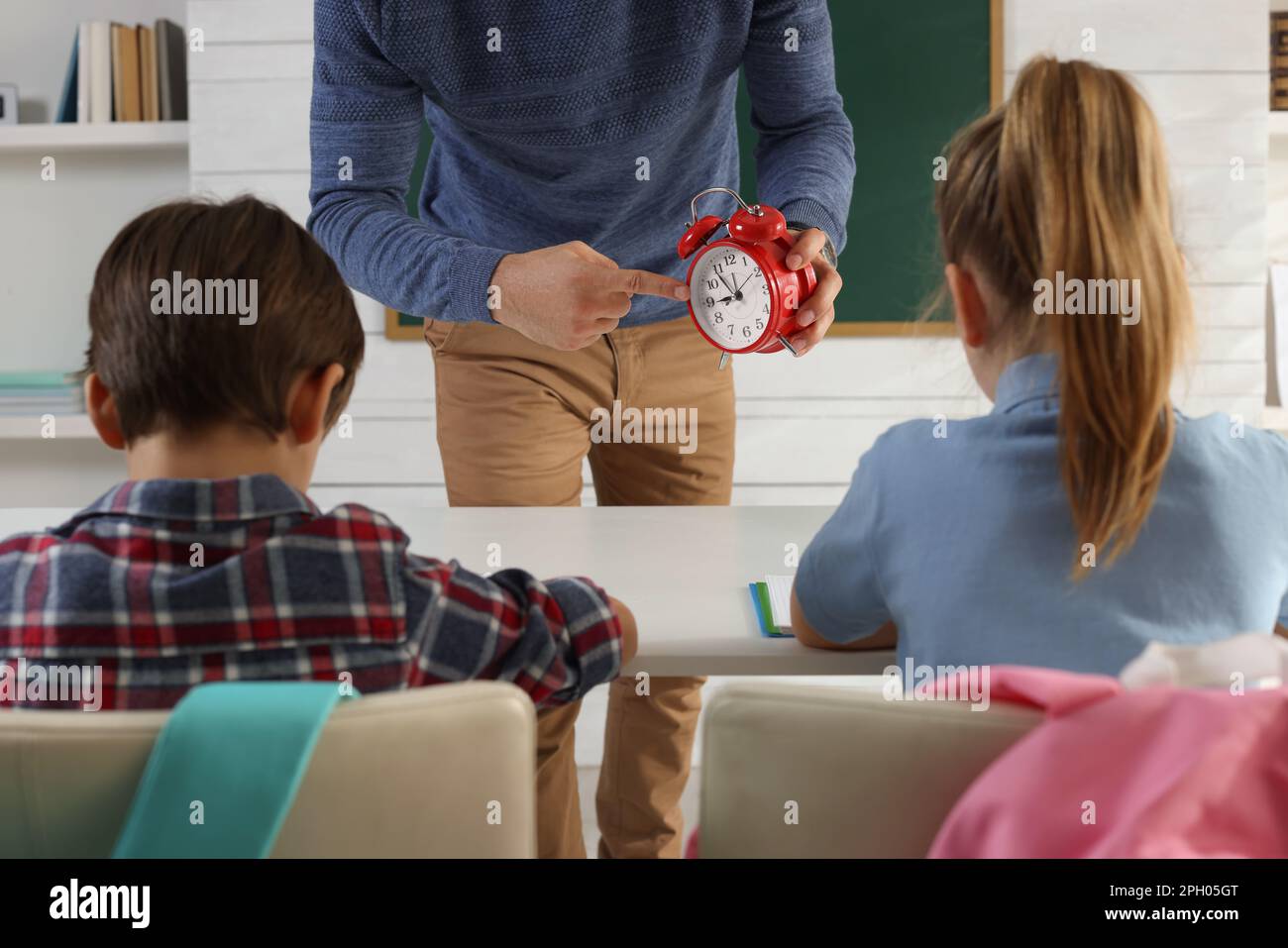 Teacher with alarm clock scolding pupils for being late in classroom