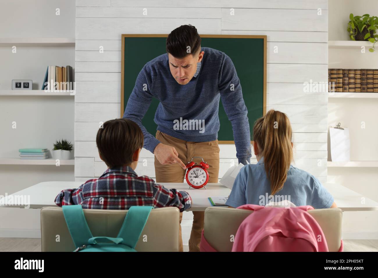 Teacher with alarm clock scolding pupils for being late in classroom