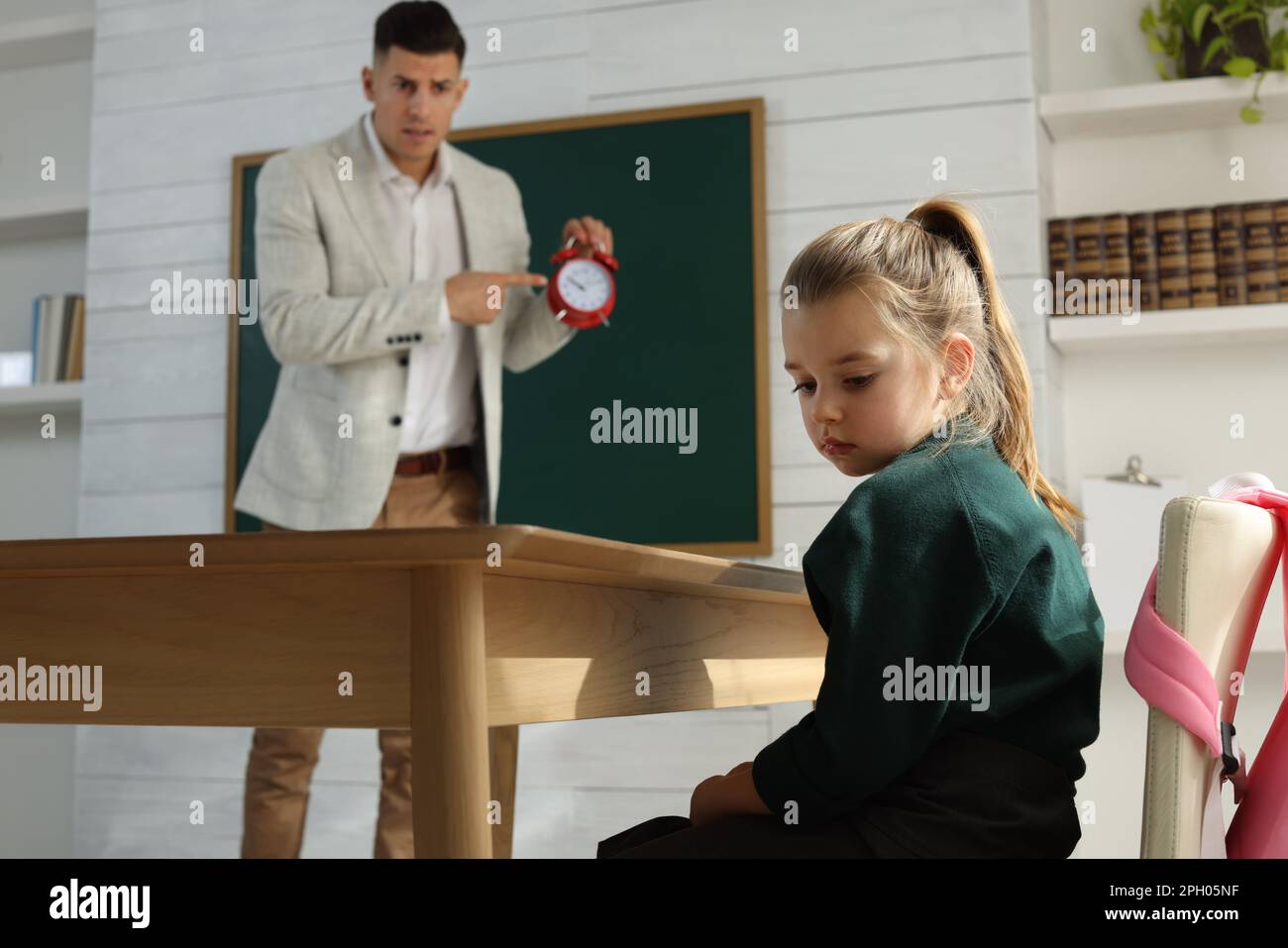 Teacher with alarm clock scolding pupil for being late in classroom