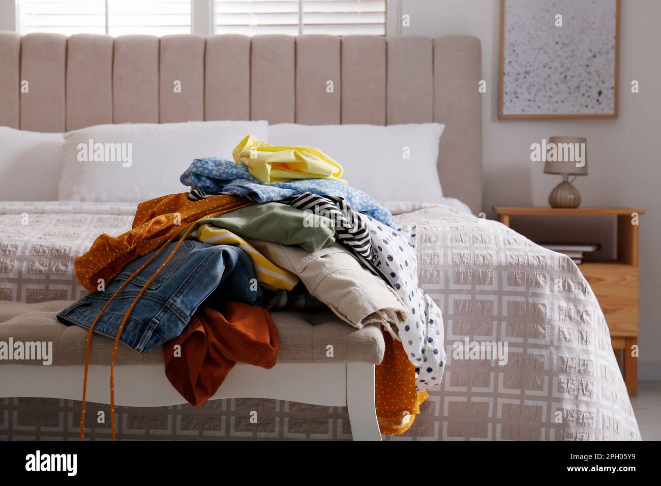 Messy pile of dirty clothes on indoor bench in bedroom. Tidying up method Stock Photo