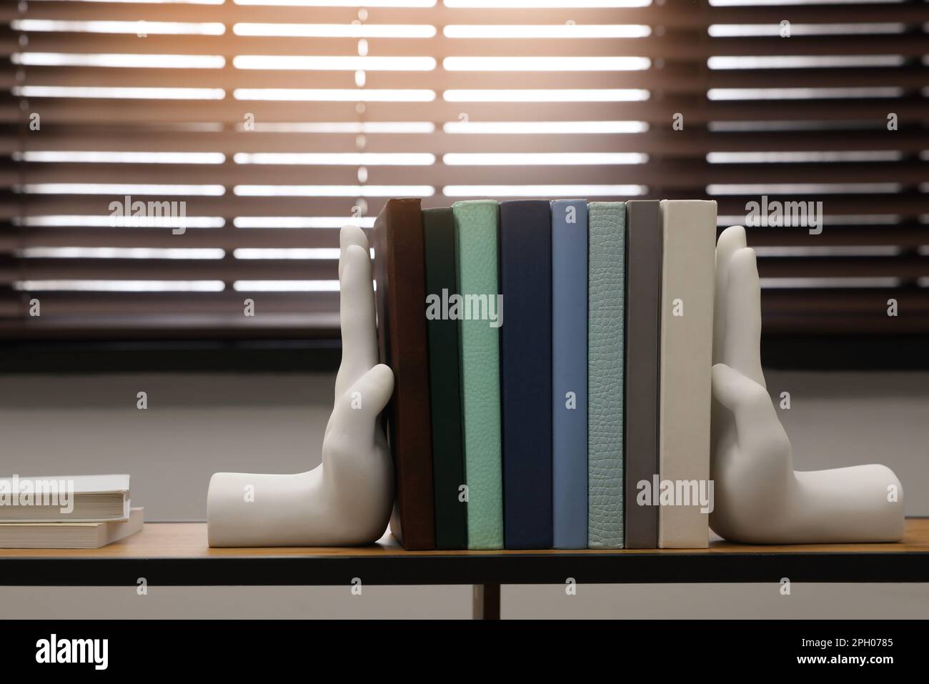 Beautiful hand shaped bookends with books on shelf indoors Stock Photo