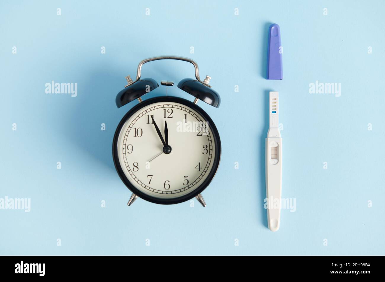 Still life with alarm clock and pregnancy test at work appearance of two stripes on blue