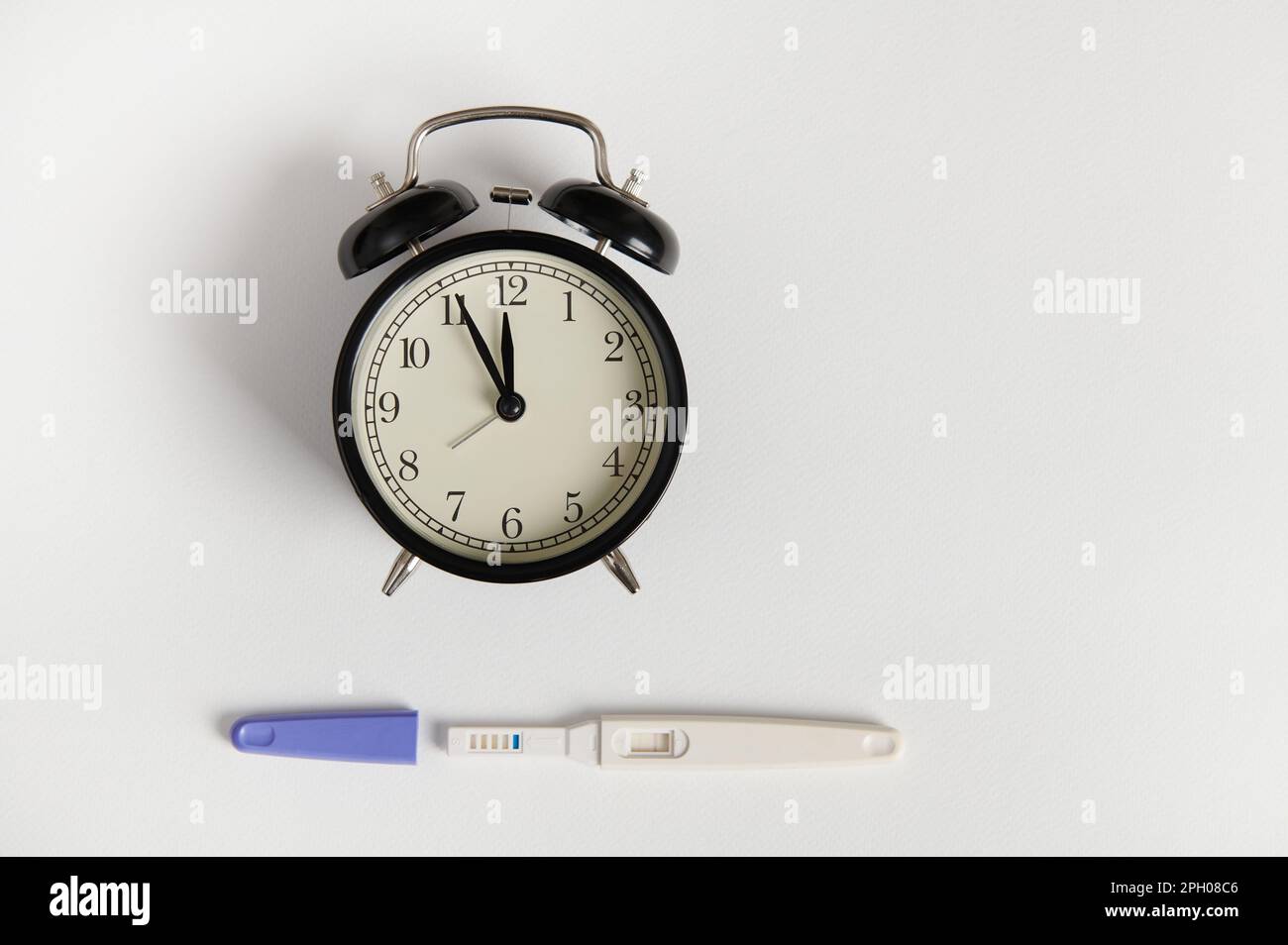 Flat lay with alarm clock and positive pregnancy test kit on white