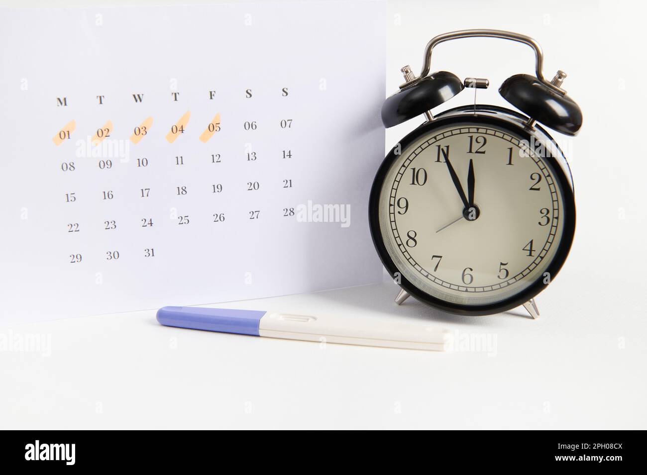 Still life with pregnancy test, black alarm clock and a white calendar