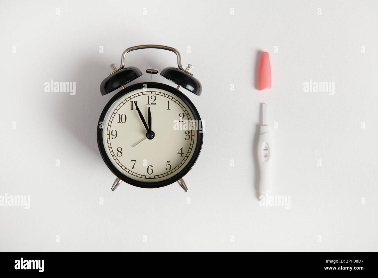 Still life with black vintage alarm clock and inkjet positive pregnancy