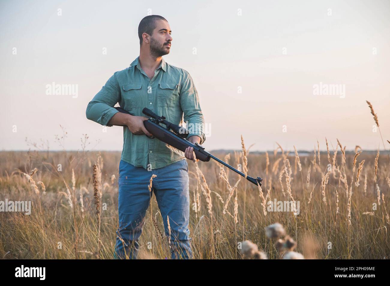 man with a rifle with a telescopic sight stands in a field Stock Photo