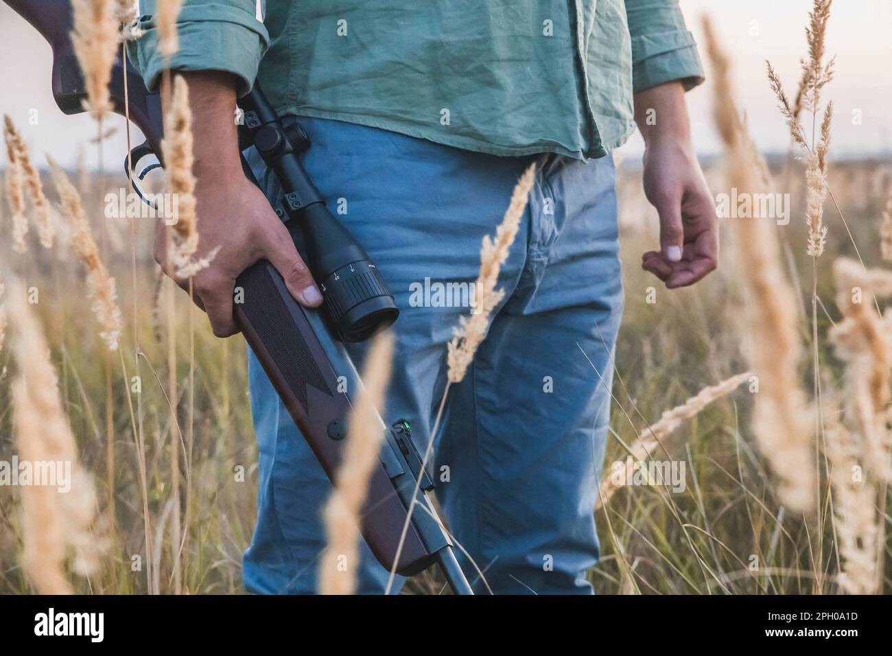 man with a rifle with a telescopic sight stands in a field Stock Photo