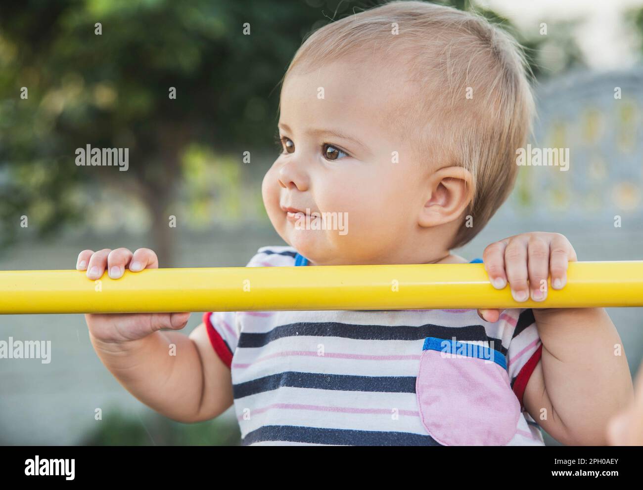 beautiful blonde baby pulls herself up on the horizontal bar Stock