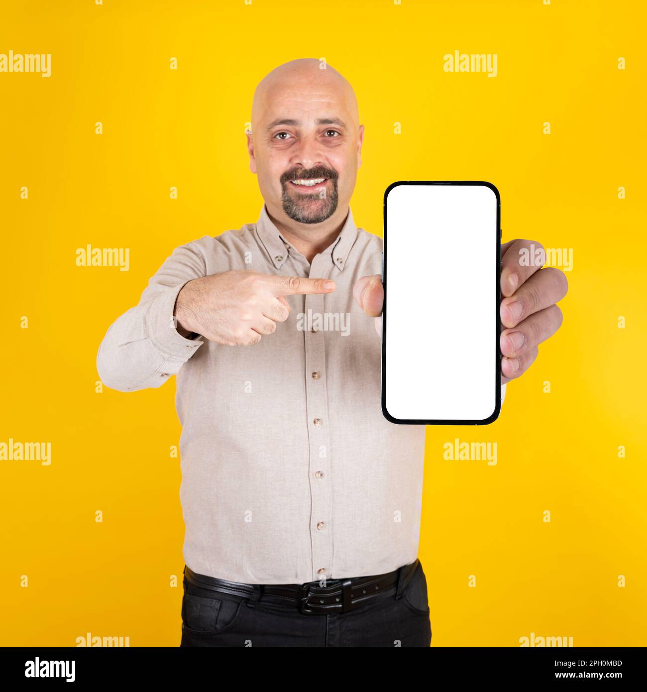 mature businessman standing over yellow background and pointing smartphone. Looking camera, smiling. Web site, application placement mockup. Stock Photo