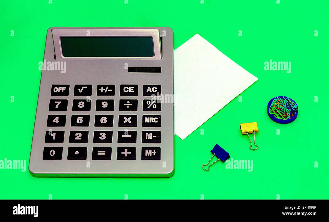 Digital electronic calculator with blank paper note and other office supply stationary like pile of colorful metal paper clips Stock Photo