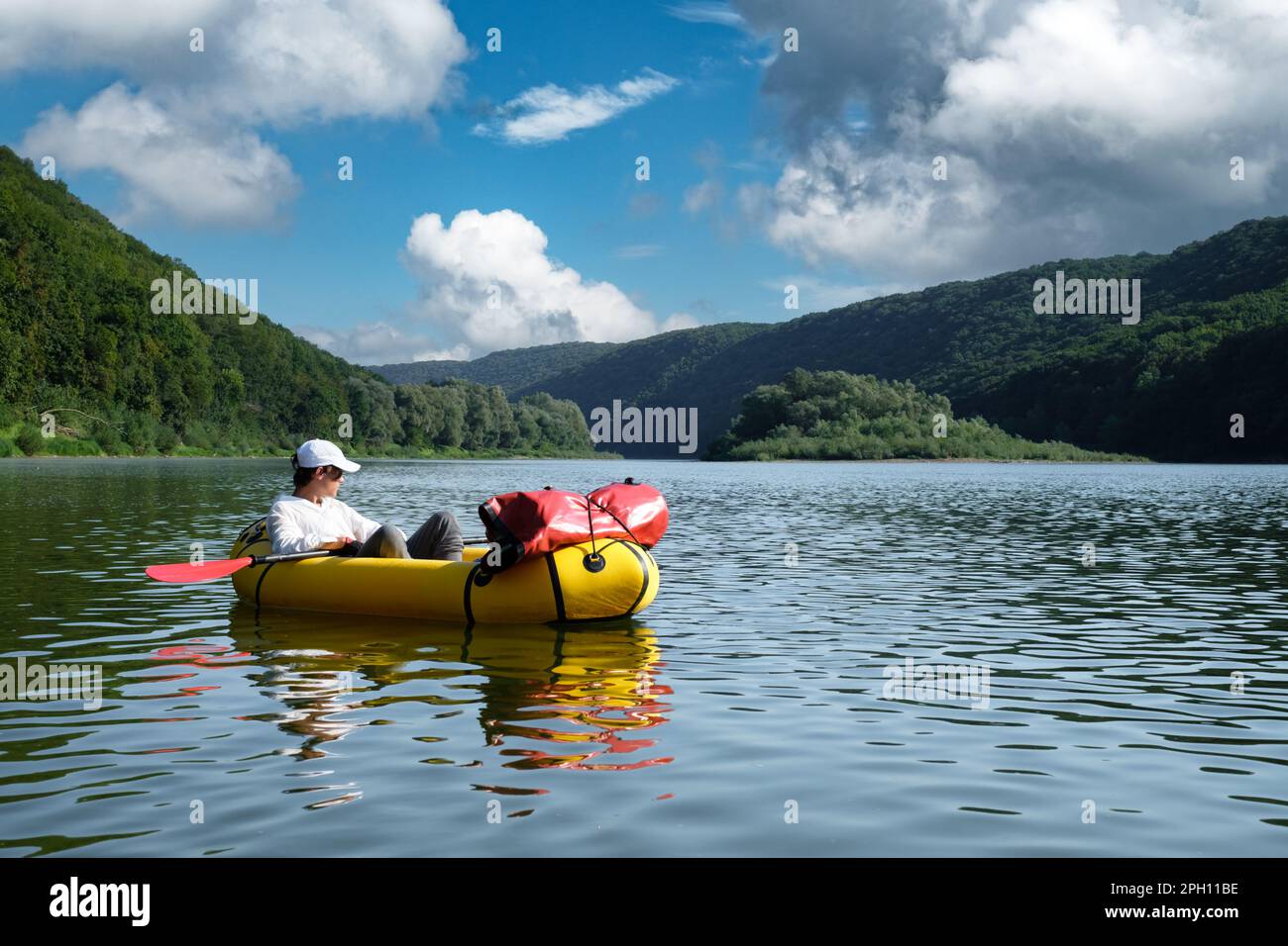 Tourist in white shirt on yellow packraft on a sunrise river. Blue sky with clouds on background. Packrafting. Active lifestile concept Stock Photo