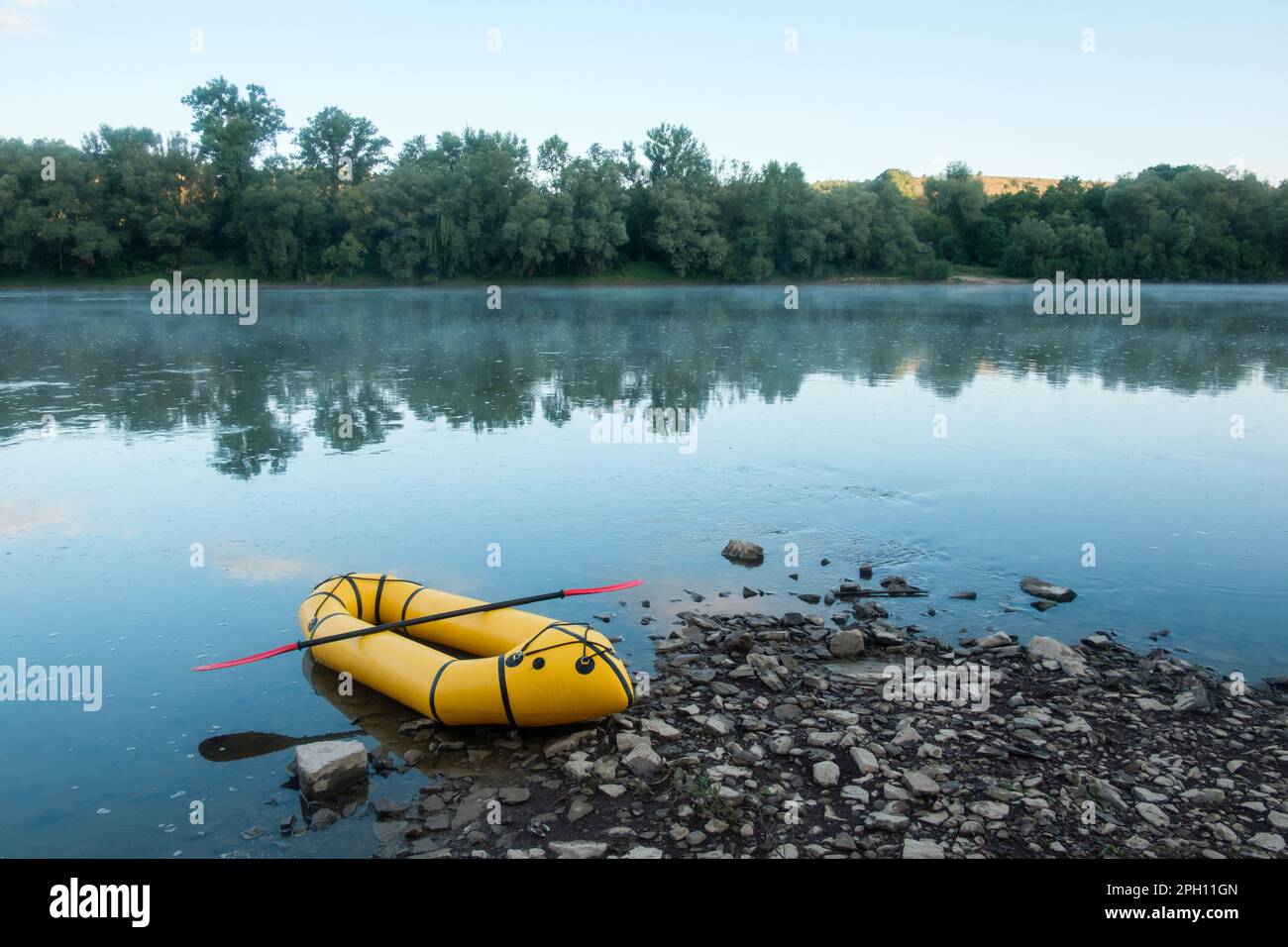 Packrafting concept with yellow packraft boat on a calm sunrise river with morning fog. Active lifestile background Stock Photo