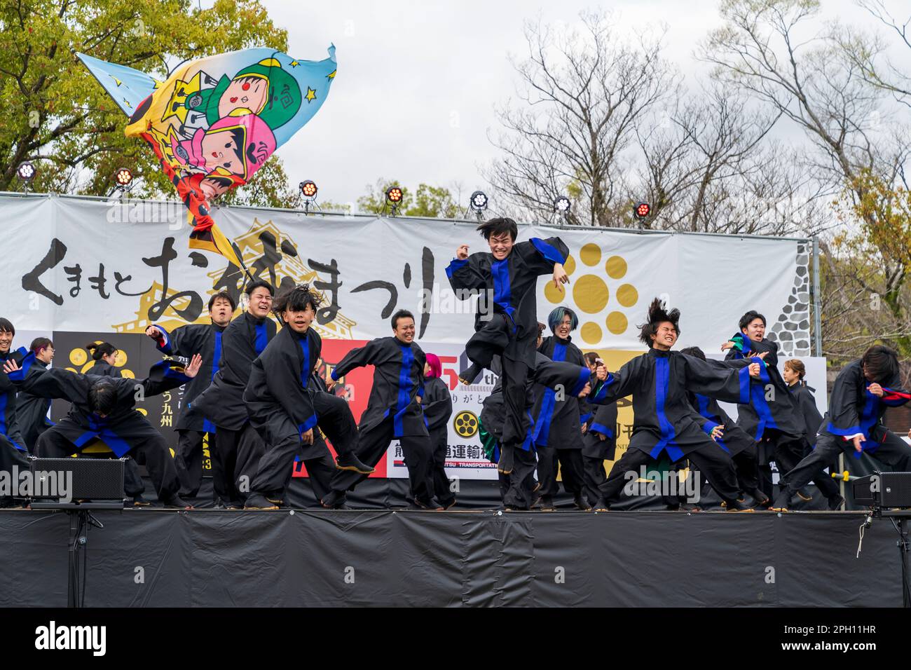 Mixed sex team of young adult Japanese dancers wearing black and blue  yukata tunics and black trousers on an outdoor stage performing Yosakoi  dancing at the annual March Kumamoto Kyusyu gassai dance