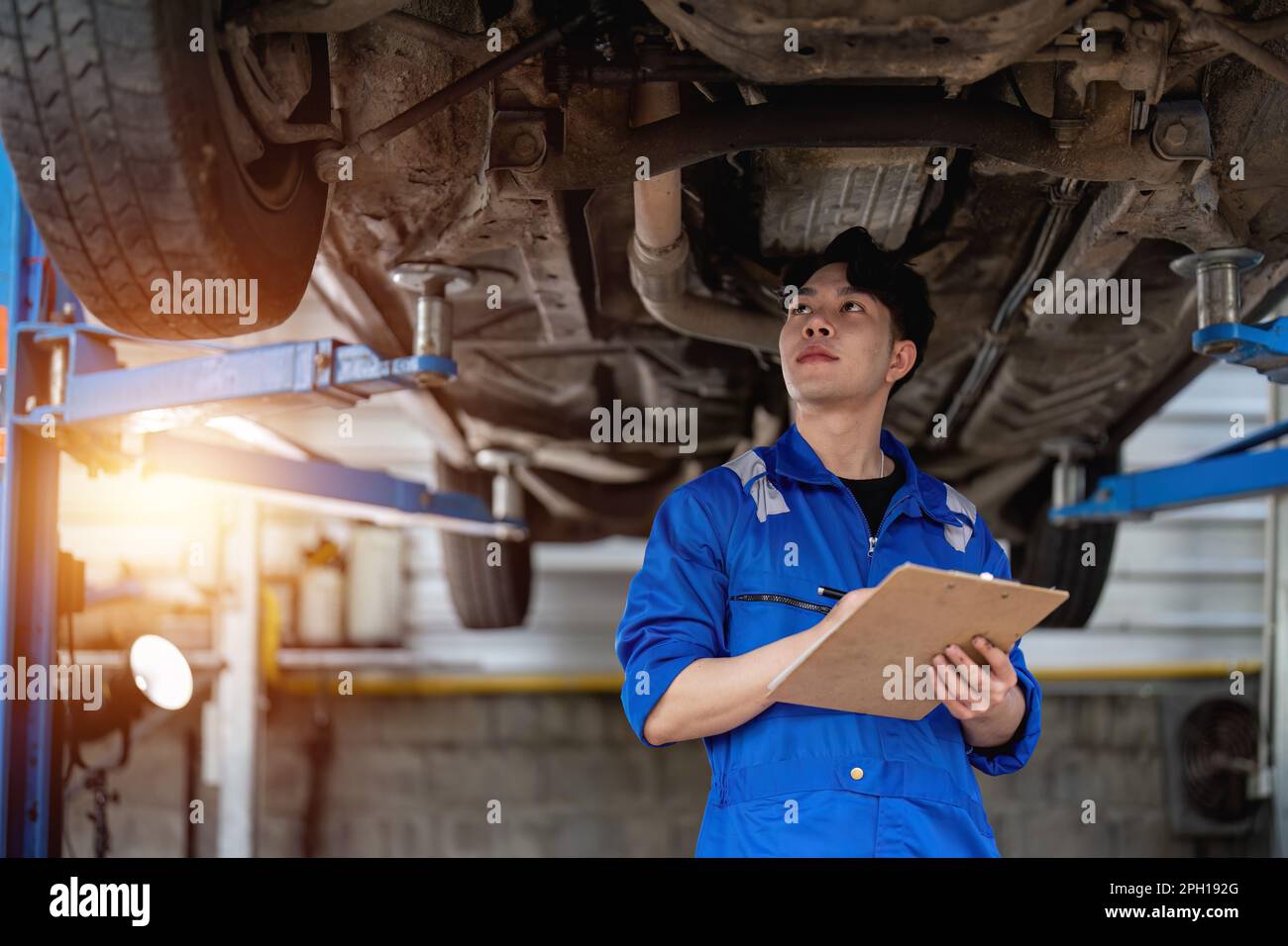 Vehicle service maintenance asian man checking under car condition in garage. Automotive
