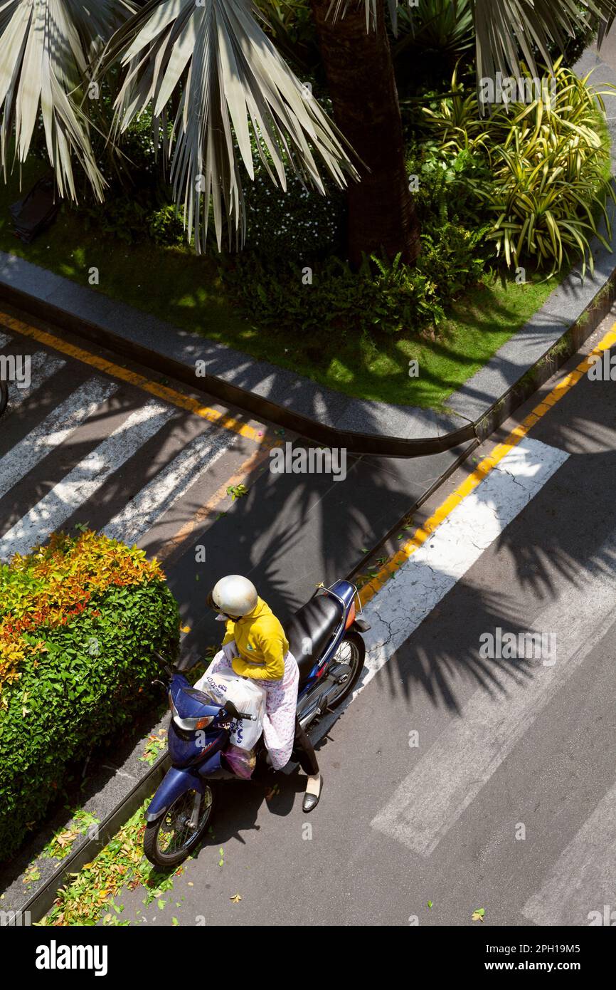 Ho Chi Minh City, Vietnam - March 16, 2023: Vietnamese woman on a motorbike on a side of a road on a sunny day. A lady diving a motorcycle stopped on Stock Photo