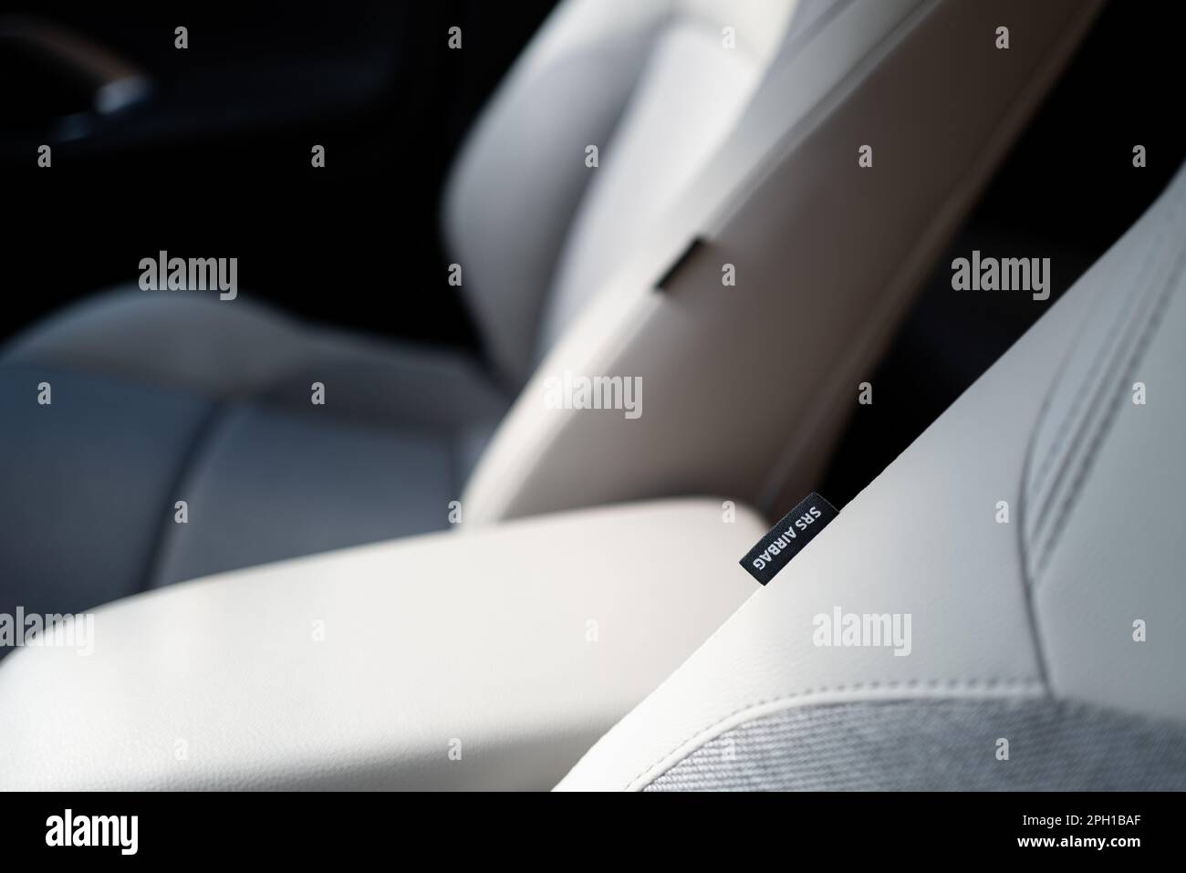 Shallow focus of an SRS Airbag tag seen attached to front part leather seats in a hybrid, new technology vehicle. The central armrest can also be seen Stock Photo