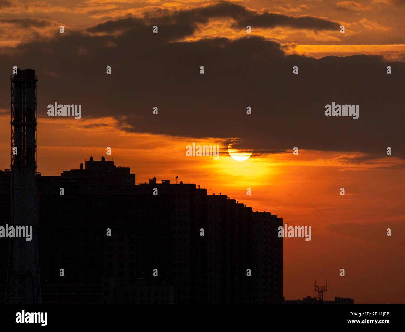 Sunset in the big city between buildings and transmission towers in the shadow with the big sun in the background. Stock Photo