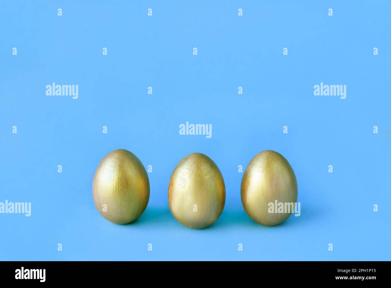 Easter eggs on blue background. Three golden eggs. Minimal style. Easter decorations. Happy Easter. Stock Photo