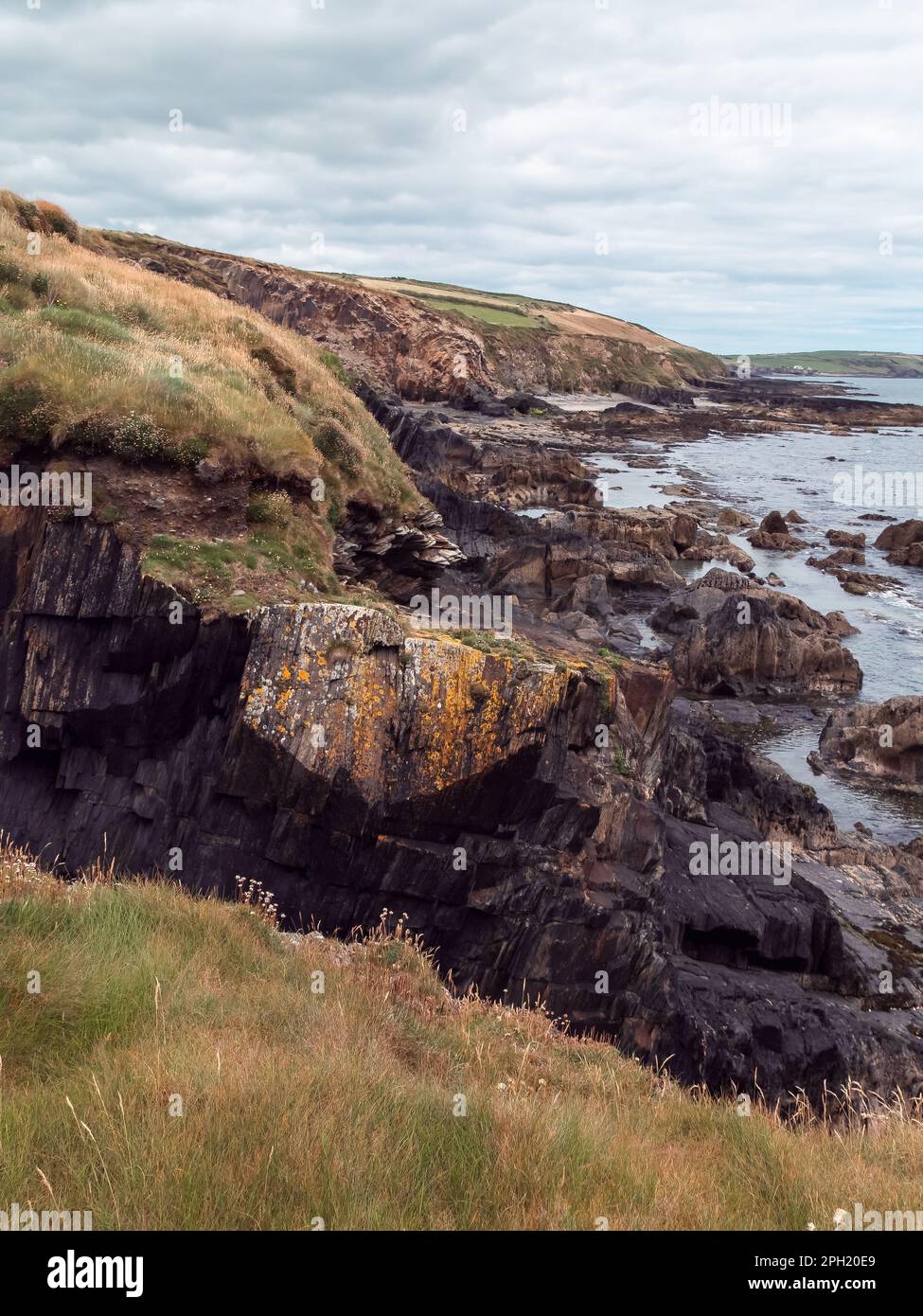 Picturesque landscape. Wild vegetation grows on stony soil. Cloudy sky over the ocean coast. Views on the wild Atlantic way, hills under clouds. Stock Photo