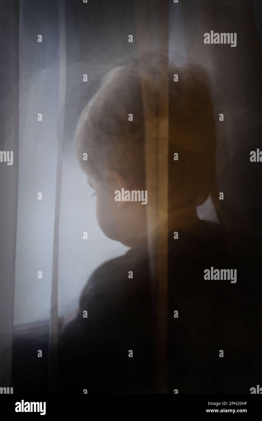 A two-year old boy looking out a window behind sheer curtains Stock ...