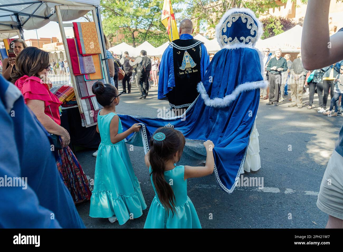 Two young girls hold the robe of La Reina (The Queen) off the ground as