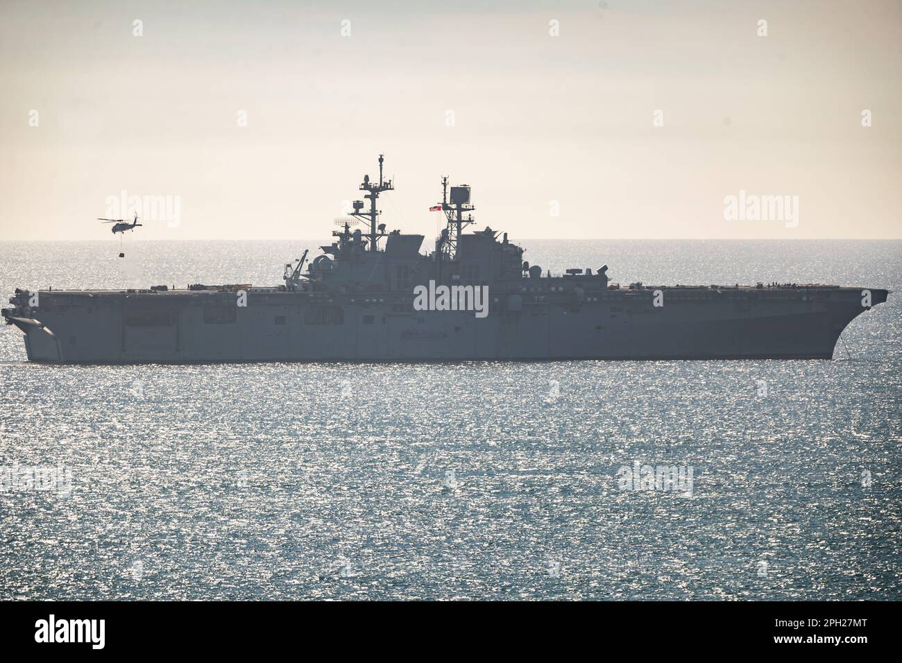 US Navy MH60S flys between a supply ship and the shoreline by Camp Pendleton along the California coast. Stock Photo