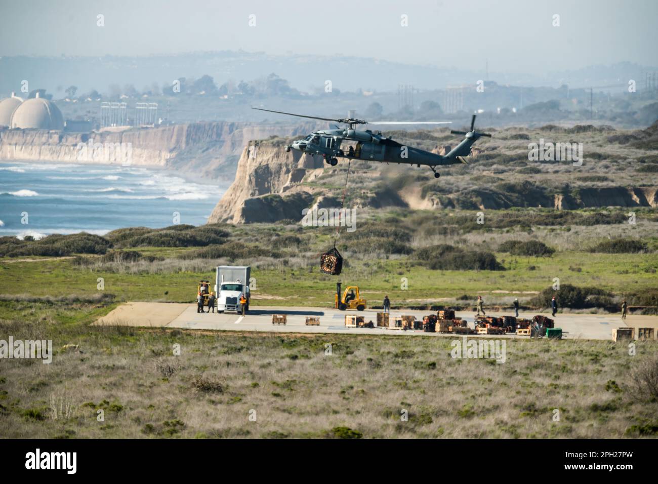 US Navy MH60S flys between a supply ship and the shoreline by Camp Pendleton along the California coast. Stock Photo