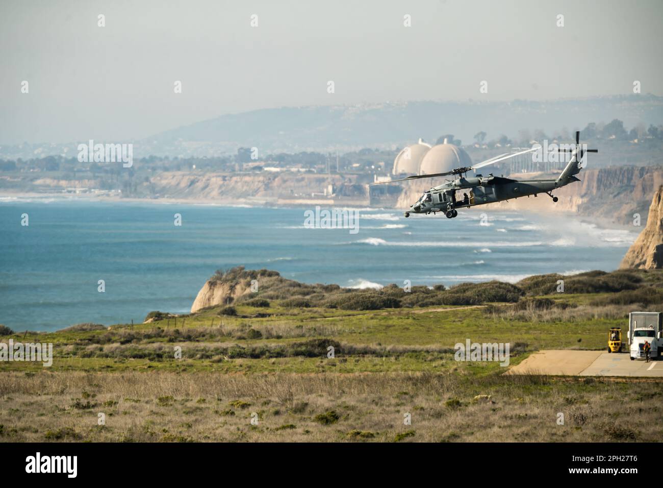 US Navy MH60S flys between a supply ship and the shoreline by Camp Pendleton along the California coast. Stock Photo
