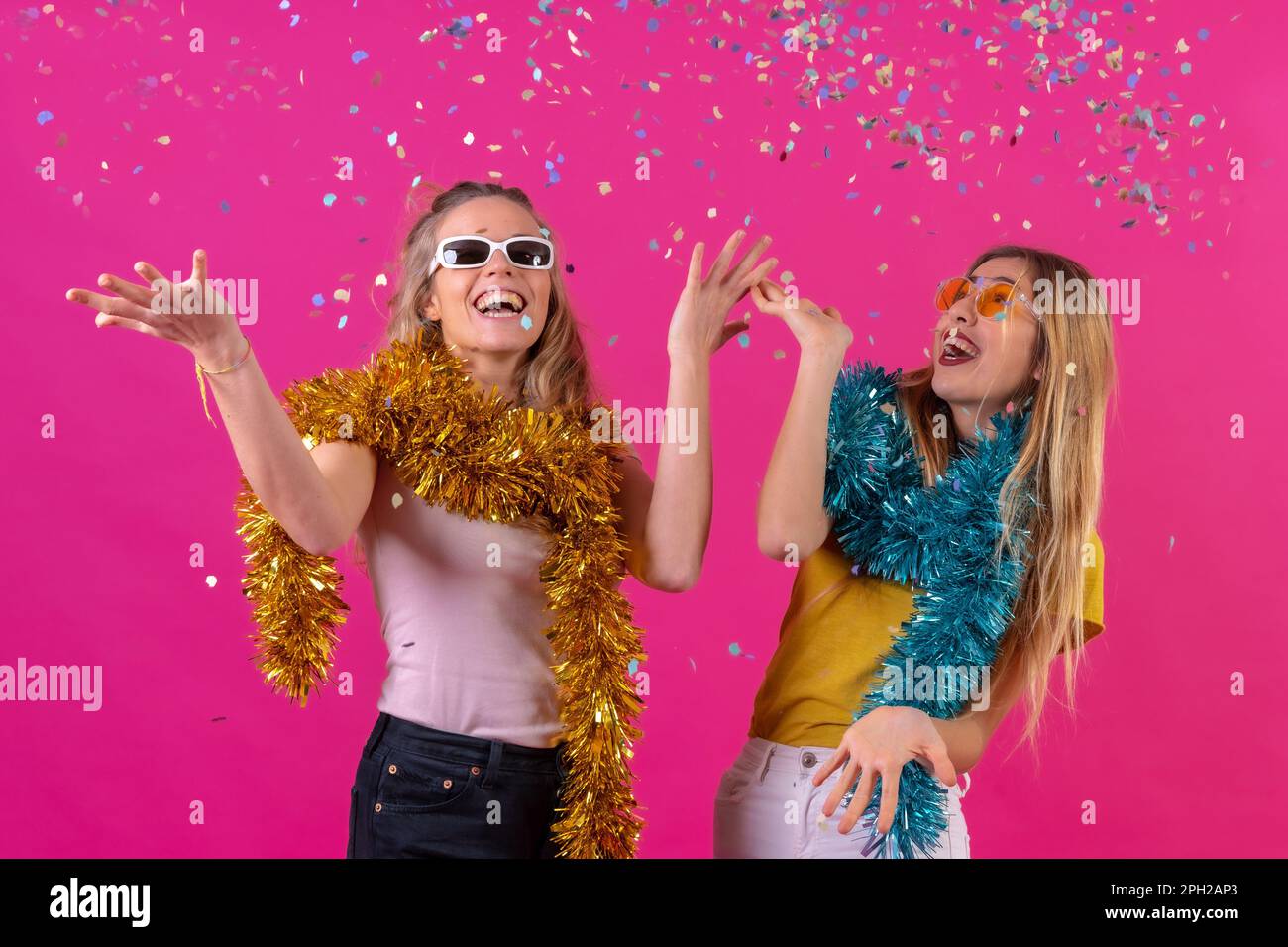 Two females wearing eyeglasses celebrating a momentous occasion by throwing confetti in the air Stock Photo