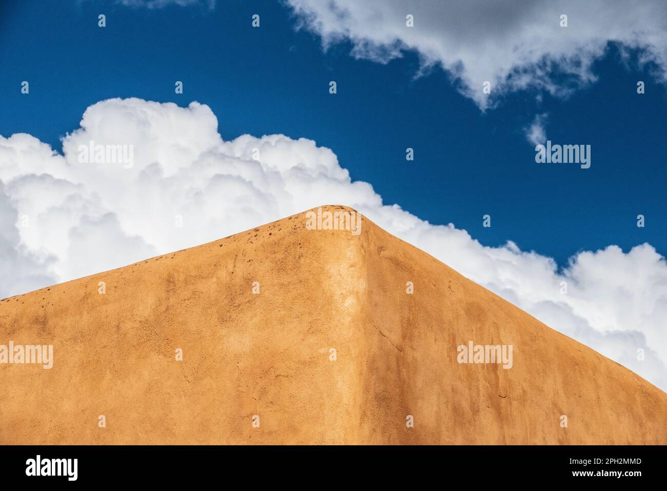 Adobe clad walls of a building in Taos New Mexico in shot against a blue sky with fluffy cumulus clouds Stock Photo