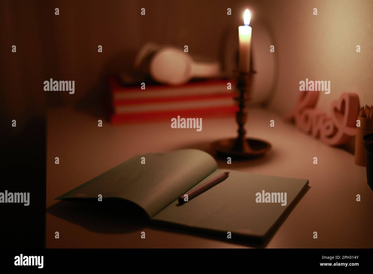 In the dark room, burning candle in candlestick is lighting on the work desk where the paper