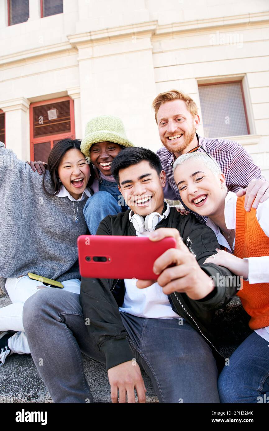 Vertical multiracial group selfie of smiling people. Young using cell phone outdoors. Social media. Stock Photo
