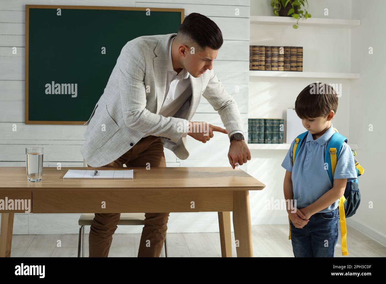 Teacher pointing on wrist watch while scolding pupil for being late in classroom Stock Photo