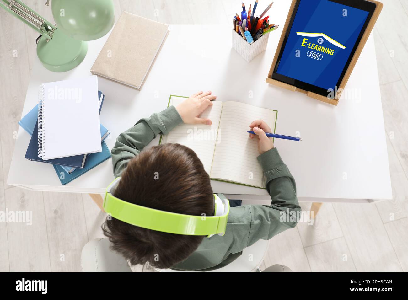 Cute little boy with modern tablet studying online at home, top view. E ...