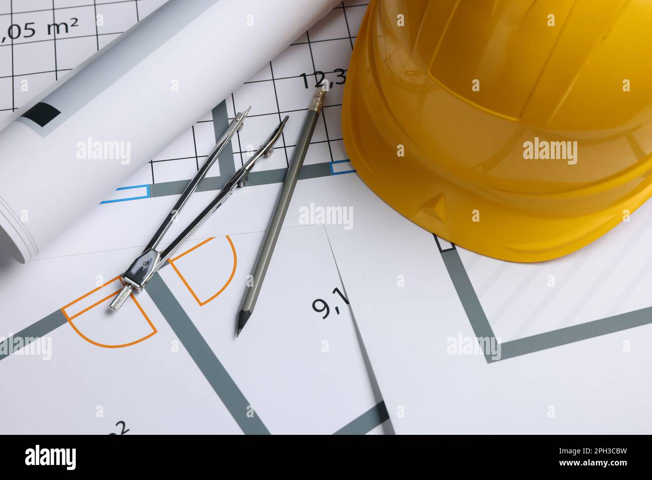 Rolled construction drawing, safety hat, pair of compasses and pencil on house plan Stock Photo