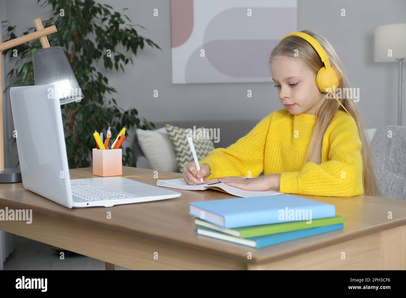 Cute little girl with modern laptop studying online at home. E-learning ...