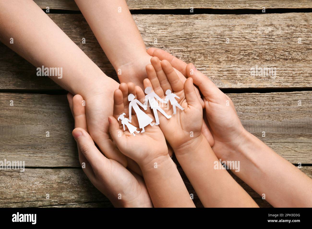 Parents and child holding paper cutout of family at wooden table, top view Stock Photo