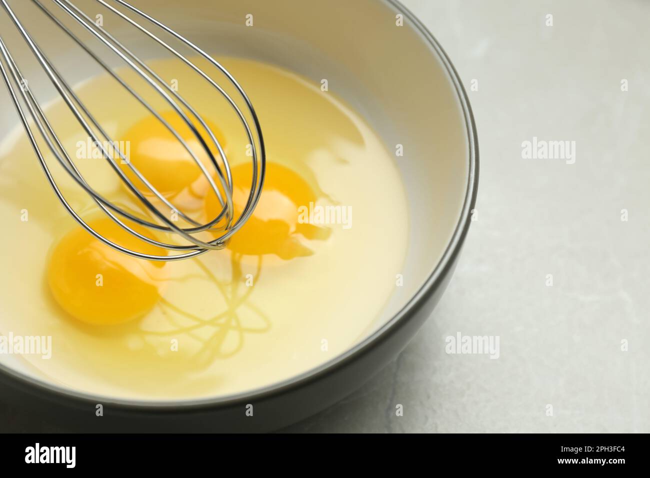 Whisking eggs in bowl on light grey table, closeup Stock Photo