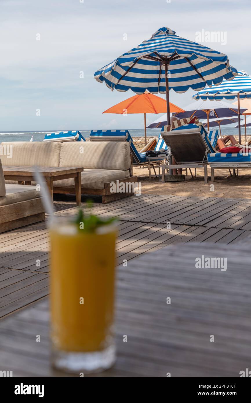 Mango juice on the beach with blue stripy imbrella on the background. Sanur, Bali, Indonesia. Vertical image. Stock Photo