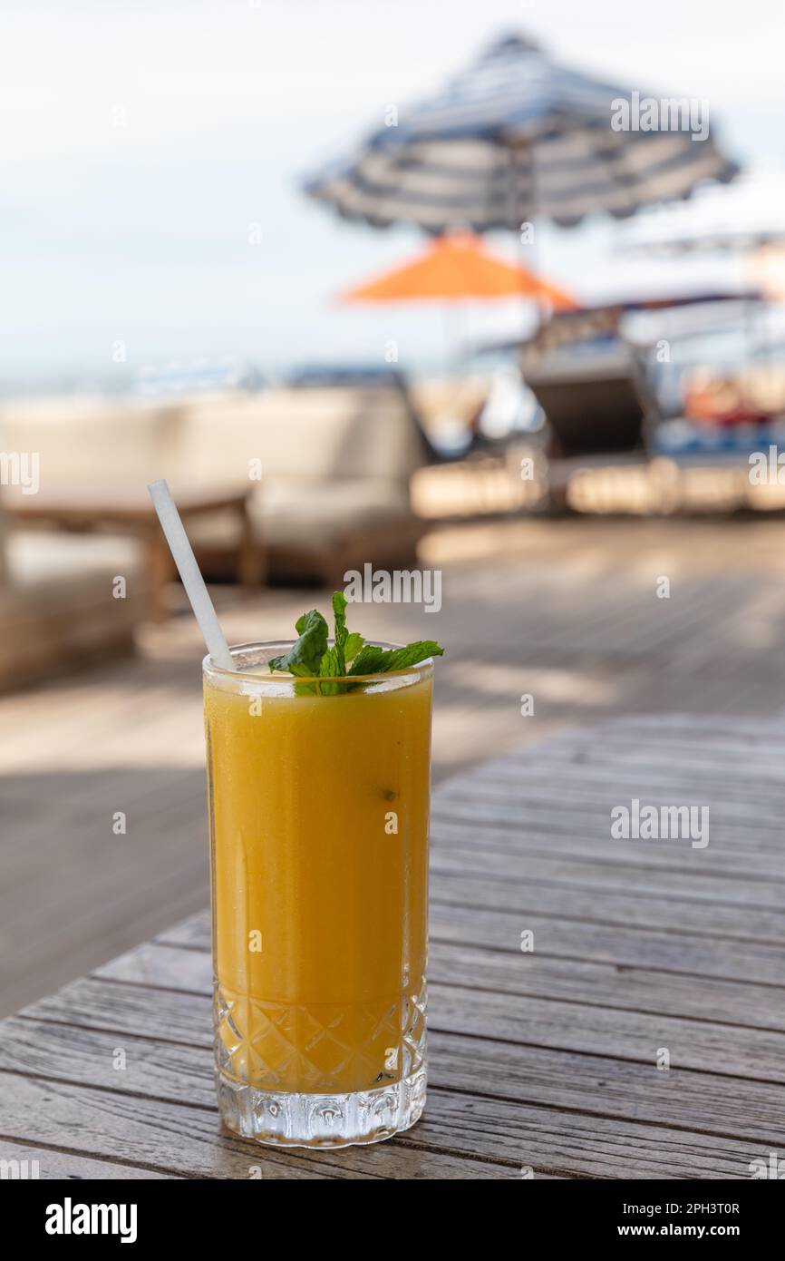 Mango juice on the beach with blue stripy imbrella on the background. Sanur, Bali, Indonesia. Vertical image. Stock Photo