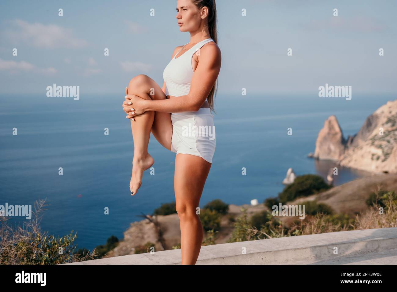 Fitness woman sea. A happy middle aged woman in white sportswear exercises morning outdoors in a park with a beach view. Female fitness pilates yoga Stock Photo