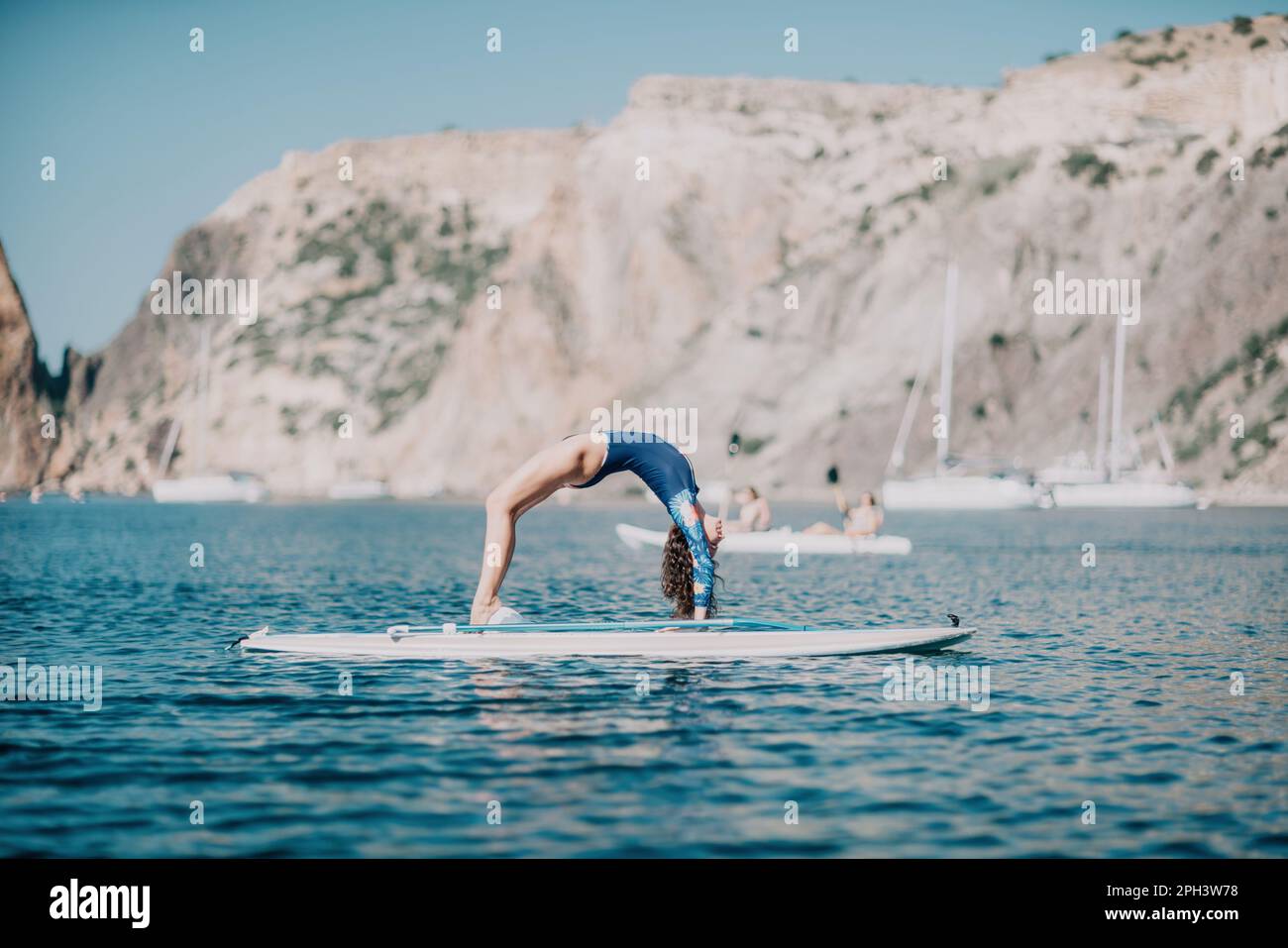 Woman sup yoga. Middle age sporty woman practising yoga pilates on paddle sup surfboard. Female stretching doing workout on sea water. Modern Stock Photo