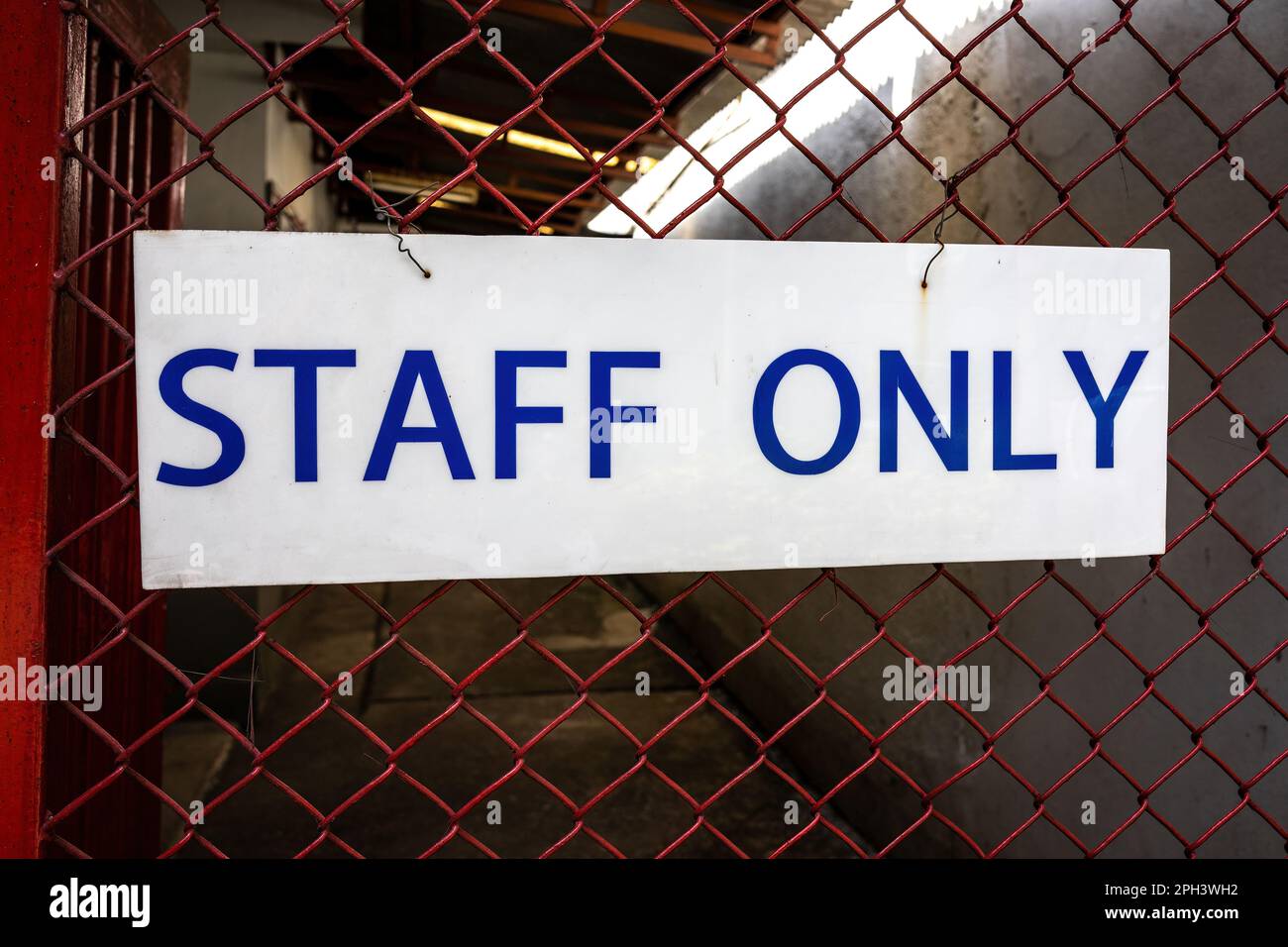 White sign in front of a red metal fence reading 'staff only' in blue. It is the demarcation to the area solely for the employees Stock Photo