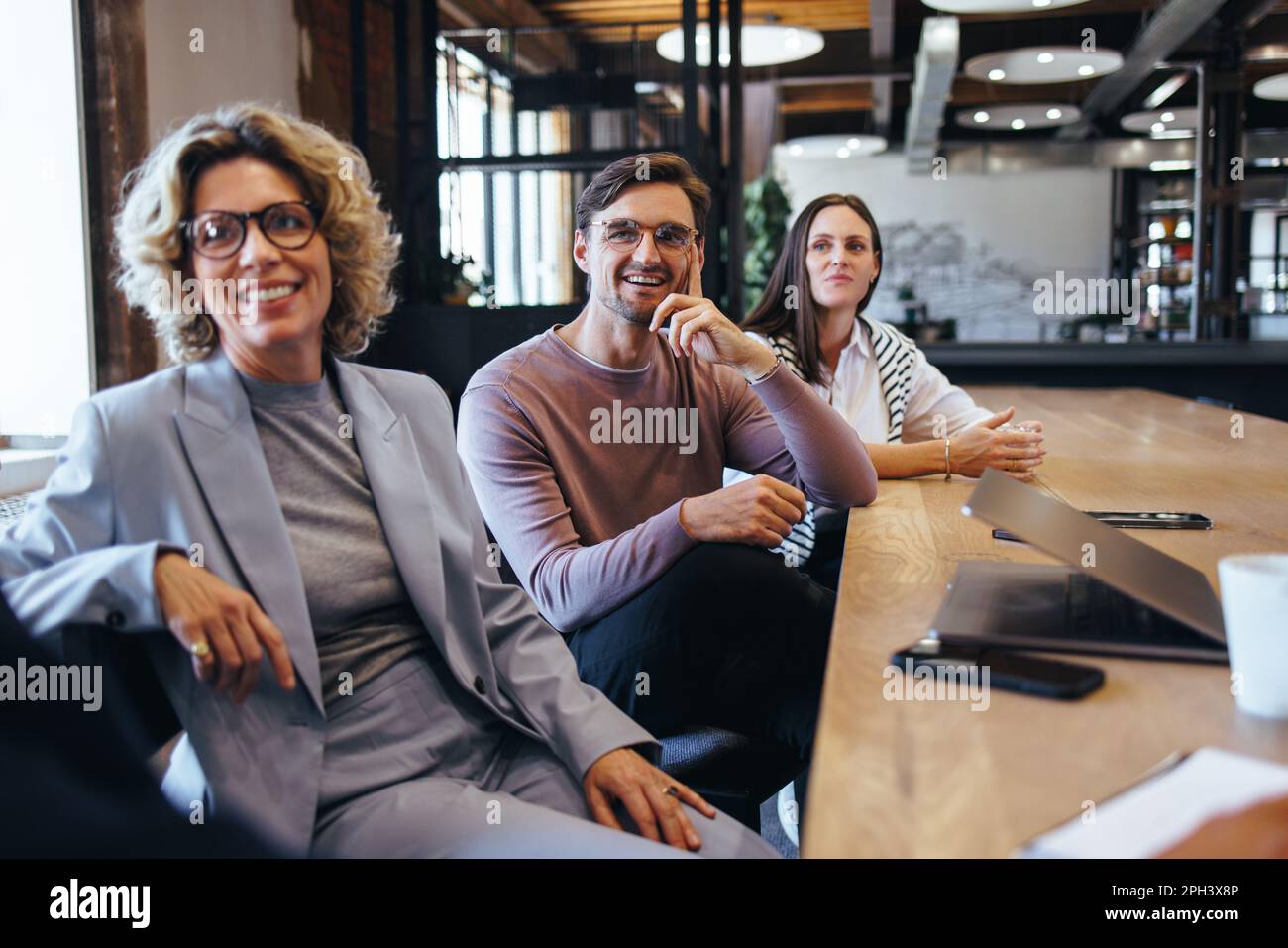 business colleagues listening to a discussion in a meeting. Team of business people sitting together in a boardroom. Happy professionals working in a Stock Photo