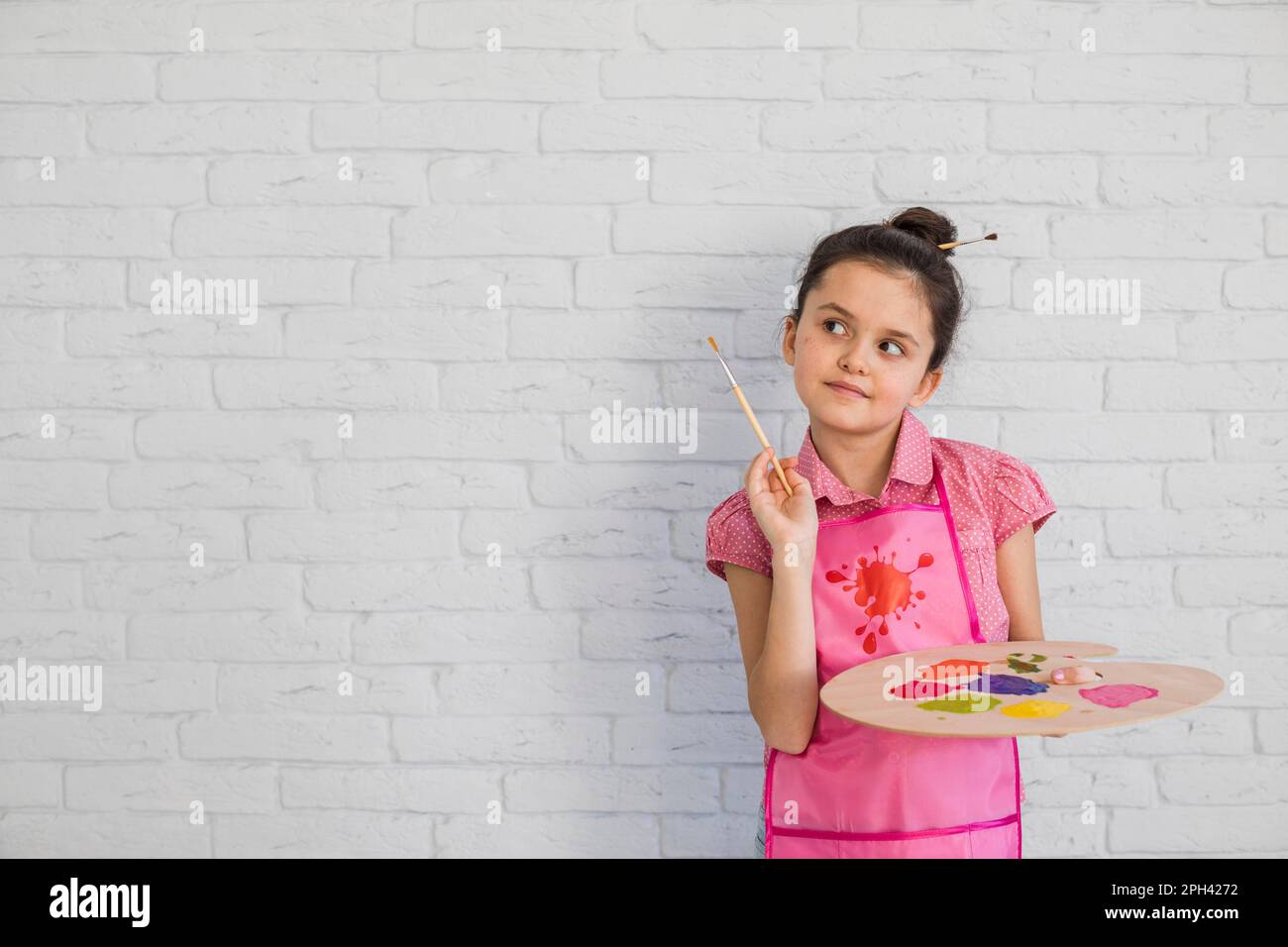 Portrait girl with paintbrush palette standing against white wall Stock Photo