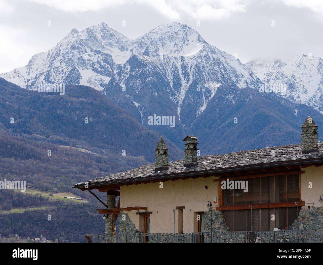 Upper part of the Les Granges Farmhouse in Nus in the Aosta Valley with the snow capped peaks of the alps behind. Italy Stock Photo