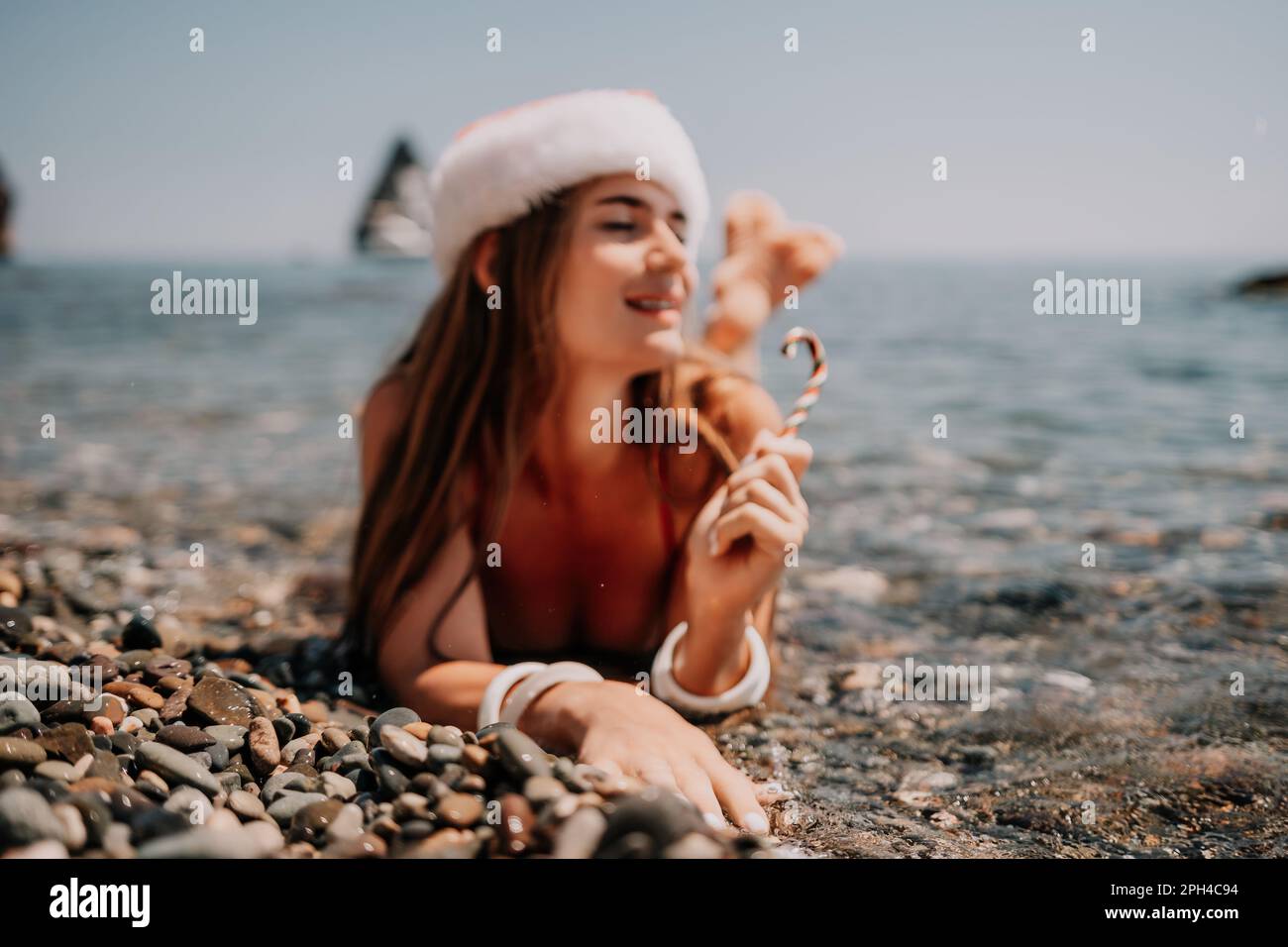 Woman travel sea. Happy tourist enjoy taking picture on the beach for memories. Woman traveler in Santa hat looks at camera on the sea bay, sharing Stock Photo