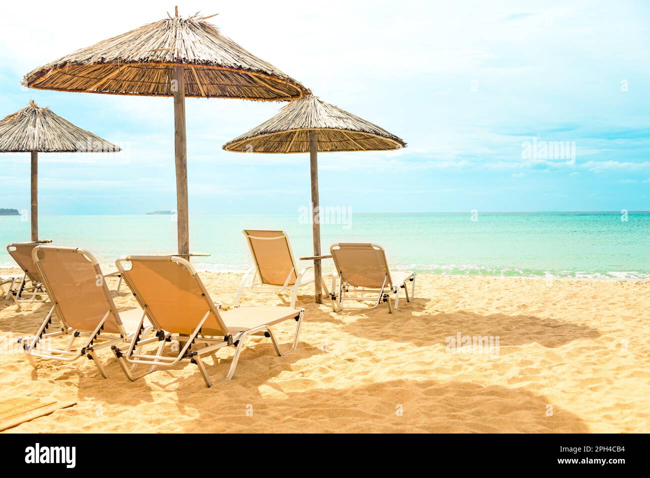 Straw umbrellas and sunbeds on a sunny golden beach seashore. Stock Photo