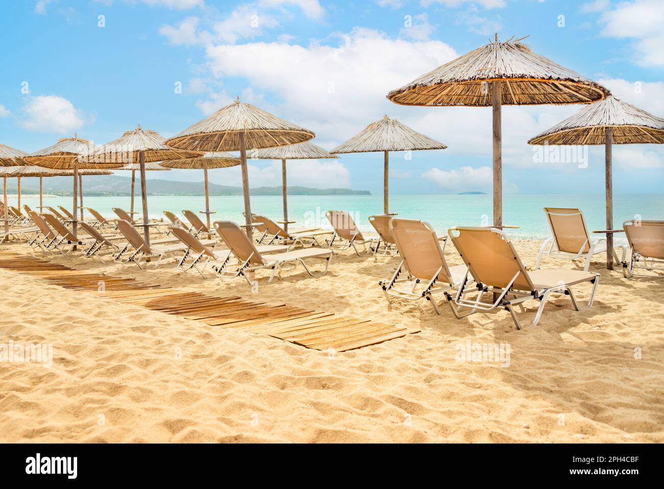 Straw umbrellas and sunbeds on a sunny golden tropical beach seashore. Stock Photo