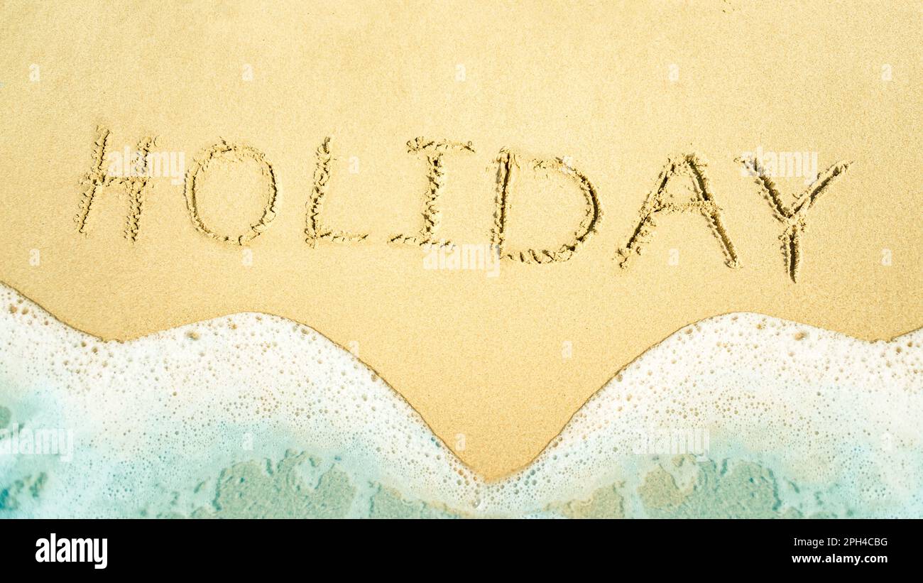 Top view of golden sand and soft wave with handwritten HOLIDAY text. Abstract summer vacation Stock Photo